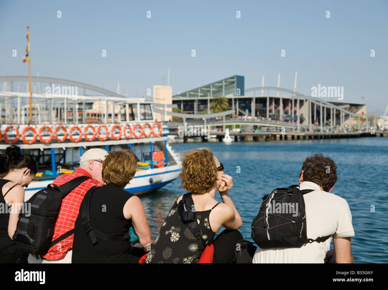 SPAIN Barcelona People sit along shore and view Maremagnum shopping and aquarium complex in Marina Port Vell Stock Photo