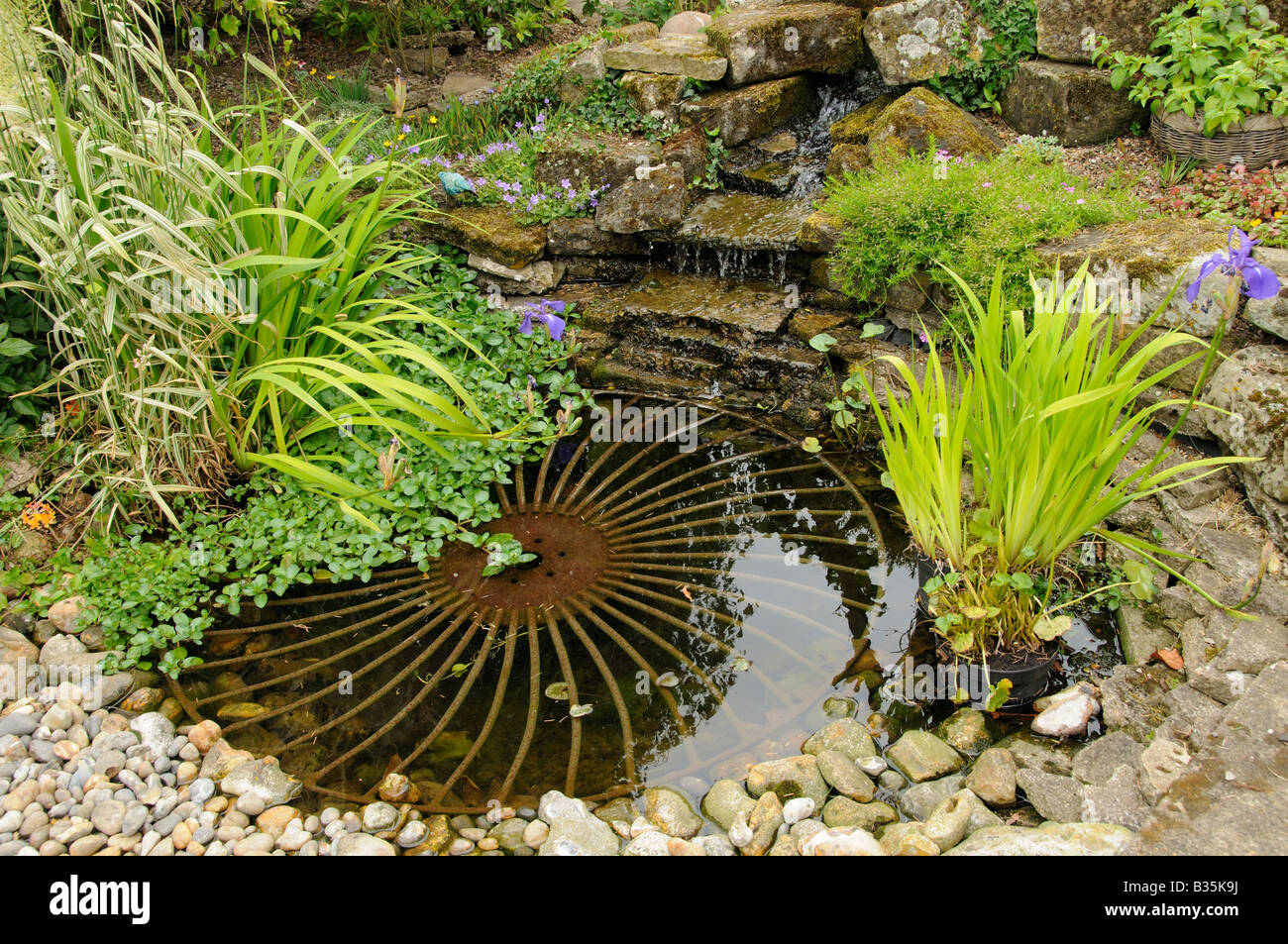 Small garden pond with rustic wheel feature and waterfall Stock Photo