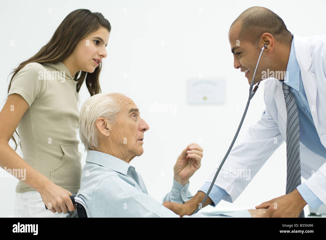 Doctor listening to senior man's heart, teen girl watching Stock Photo