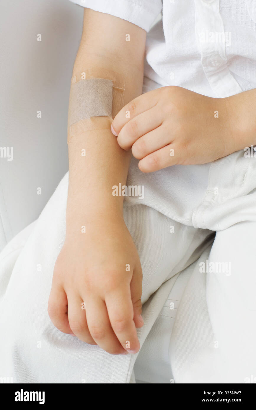 Little boy picking at adhesive bandage on his arm, cropped view Stock Photo