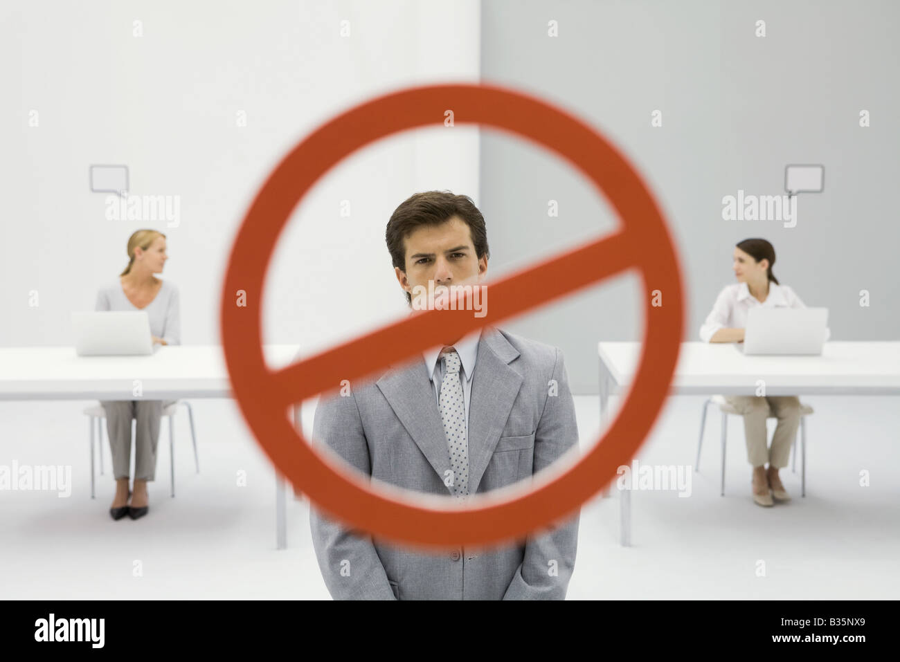 Warning sign across businessman in office, two women sitting with laptops in background Stock Photo