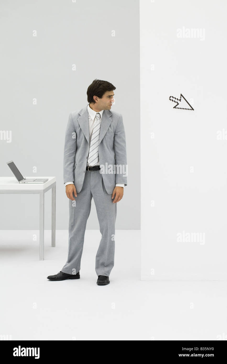 Businessman standing in office, looking at computer cursor pointing away Stock Photo