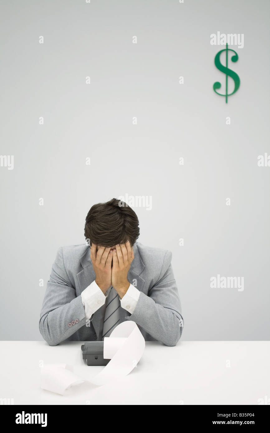 Accountant sitting with adding machine, hiding face in hands Stock Photo