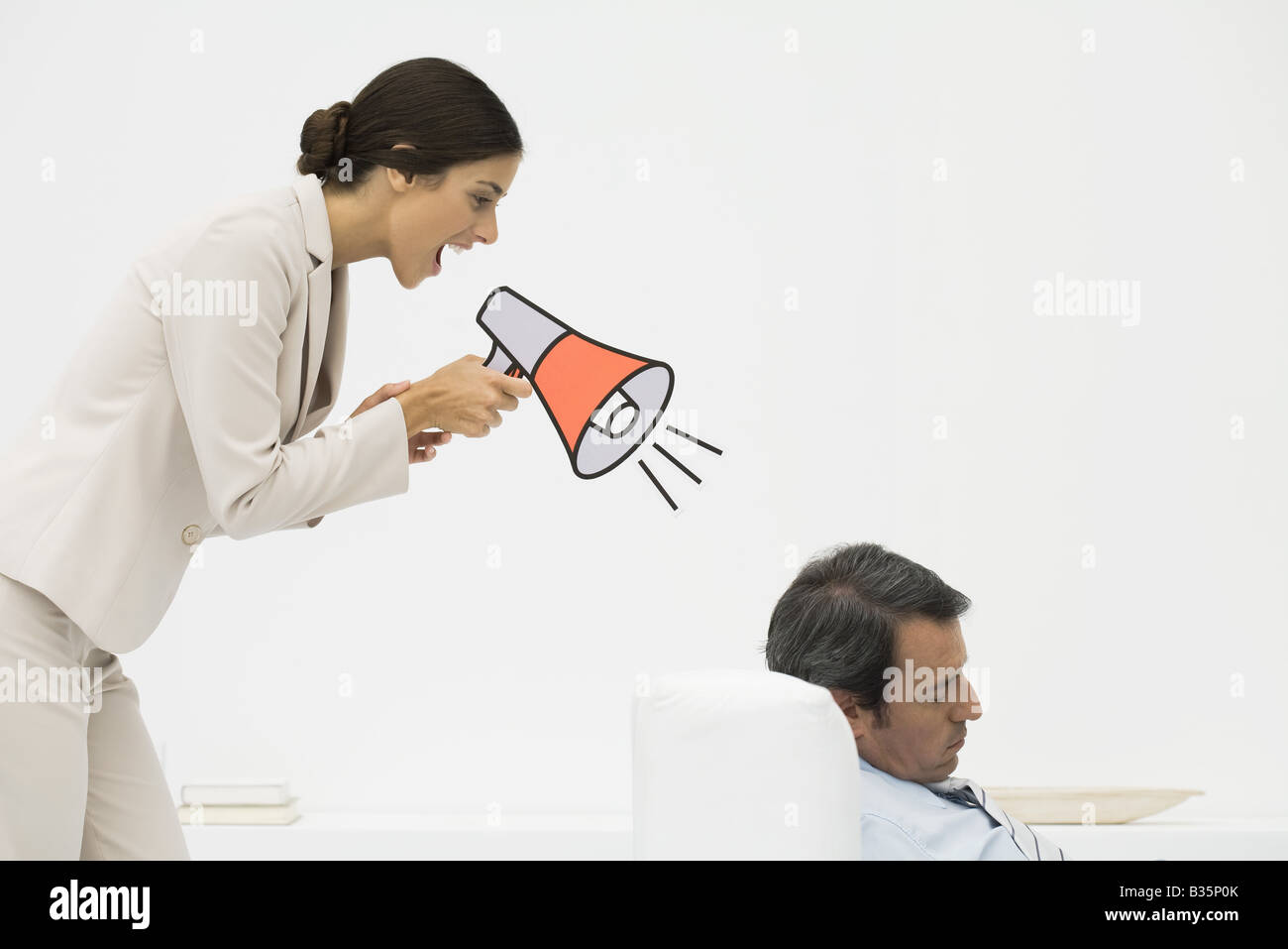 Man sleeping in chair, woman standing behind him, shouting into megaphone Stock Photo