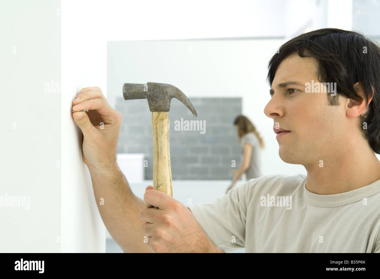 Man hammering nail into wall, woman in background Stock Photo Alamy