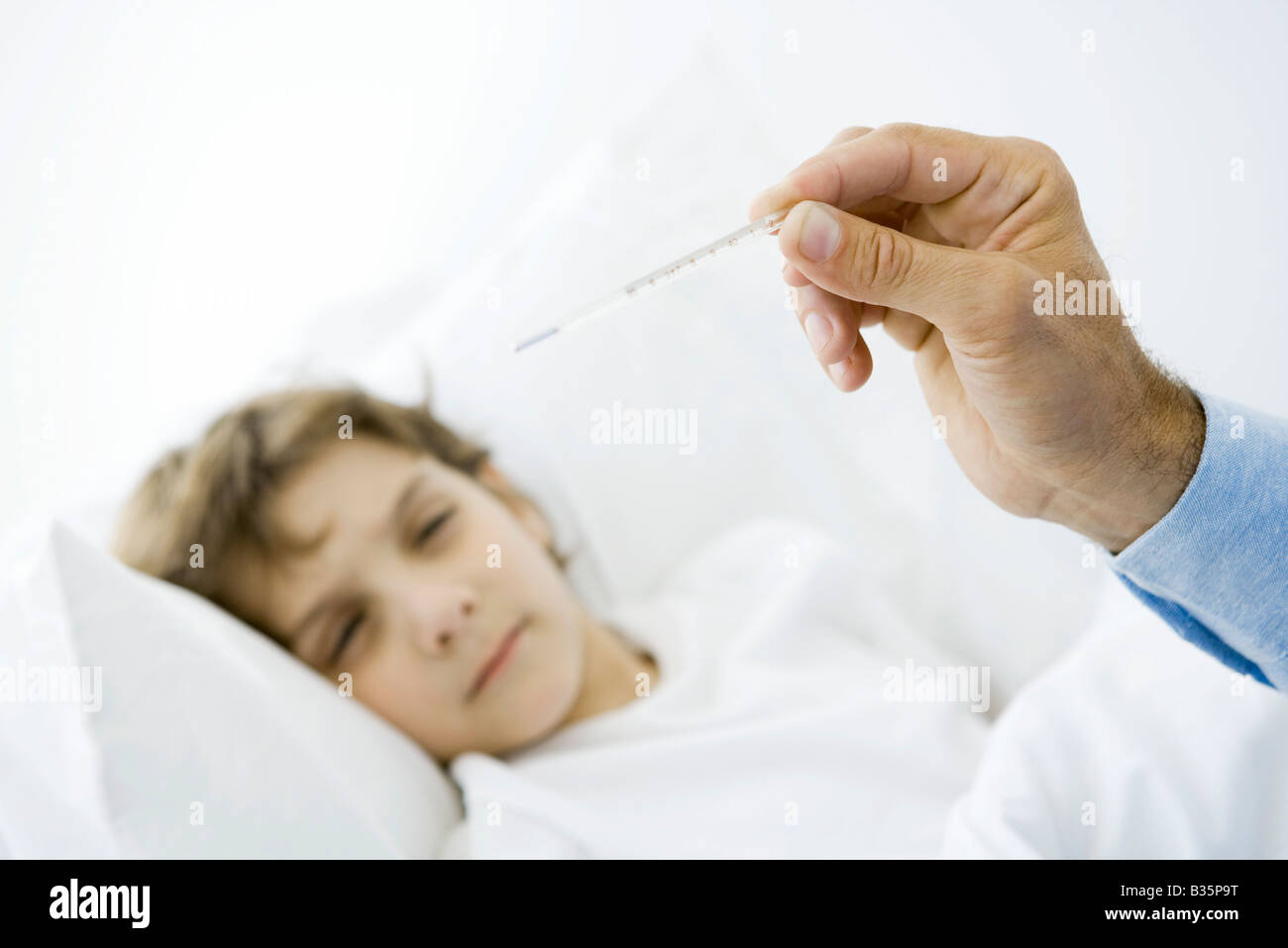 Little boy lying in bed, man's hand holding thermometer in foreground Stock Photo