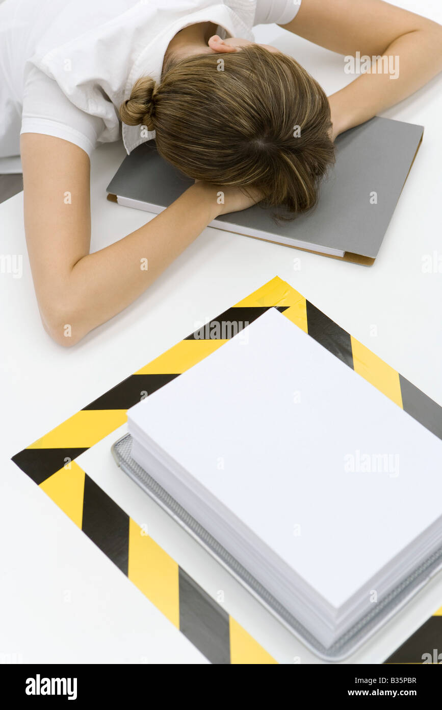 Woman sitting with her head down near a stack of paper surrounded by black and yellow tape Stock Photo