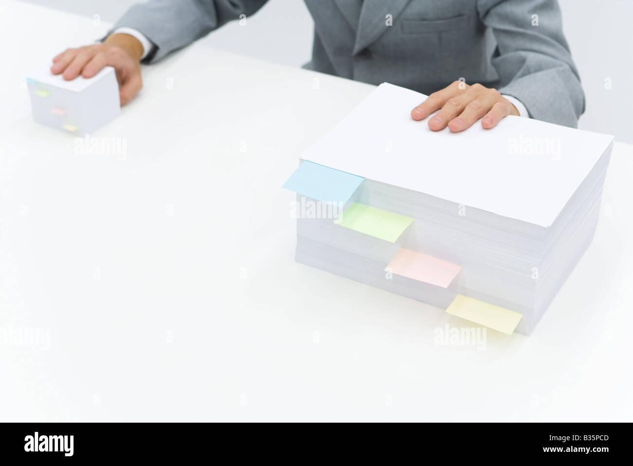 Stacks of paper with adhesive notes dividing them, man putting one hand on each stack Stock Photo