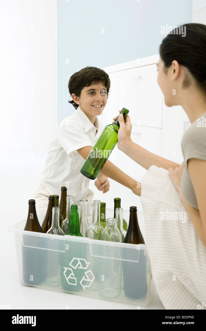 Young woman and boy placing glass bottles in recycling bin, smiling at each other Stock Photo
