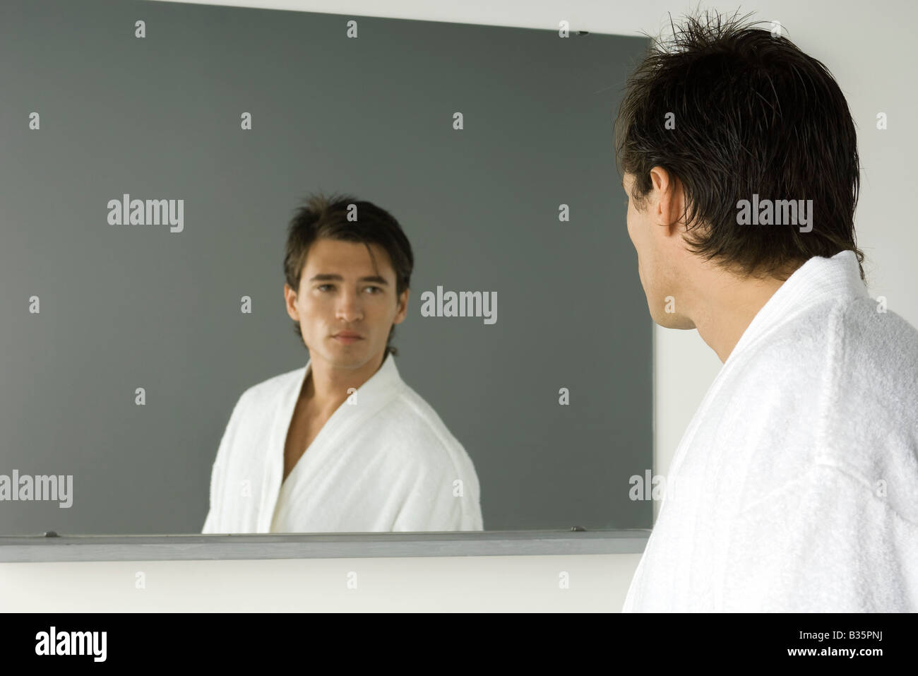 Man in bathrobe looking at self in mirror Stock Photo