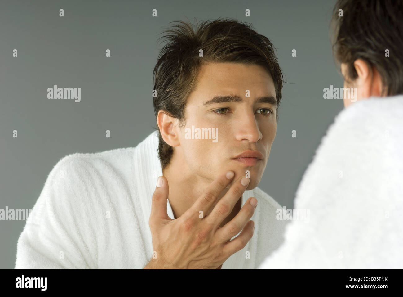 Man in bathrobe looking in mirror, inspecting skin Stock Photo