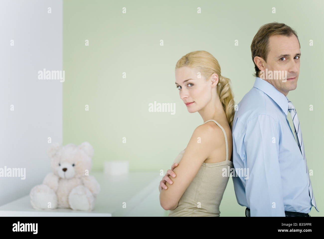 Couple standing back to back in nursery, looking over shoulders at camera, woman's arms folded Stock Photo
