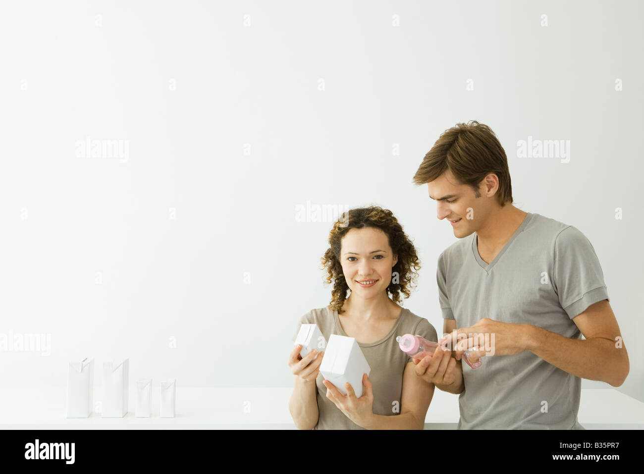New parents looking at milk cartons, man holding baby bottle, woman smiling at camera Stock Photo