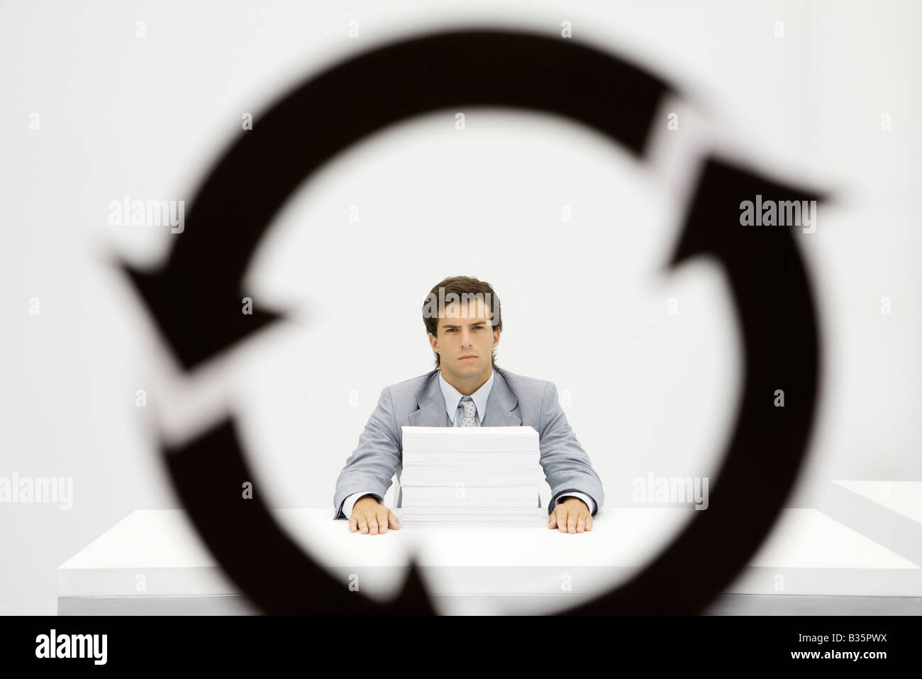 Professional sitting at desk with large stack of paper, circular arrow symbol in foreground Stock Photo