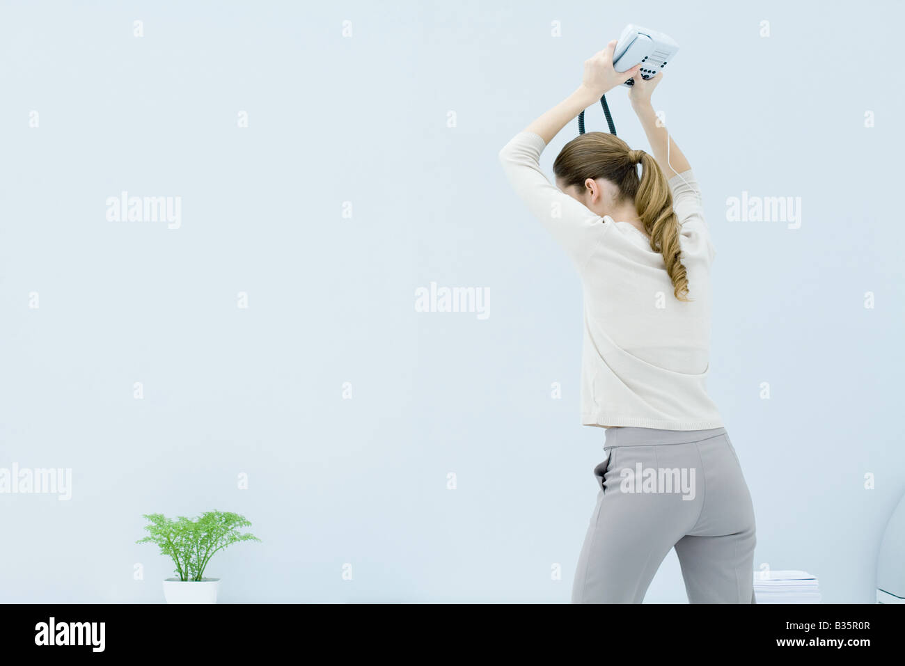Young woman holding landline phone above her head ready to smash it on the ground, rear view Stock Photo