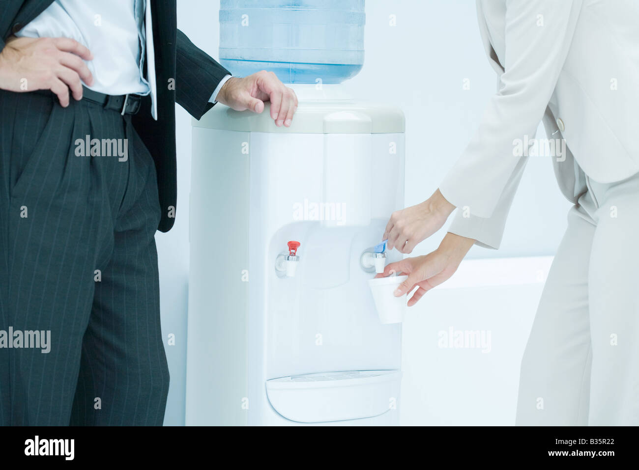 Professional woman filling disposable cup with water from water cooler