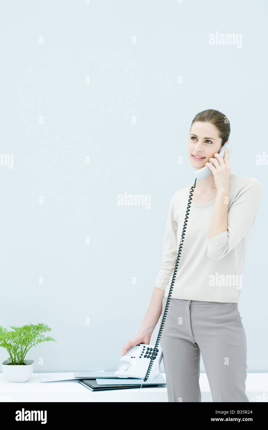 Woman standing and talking on landline phone, looking away and smiling Stock Photo
