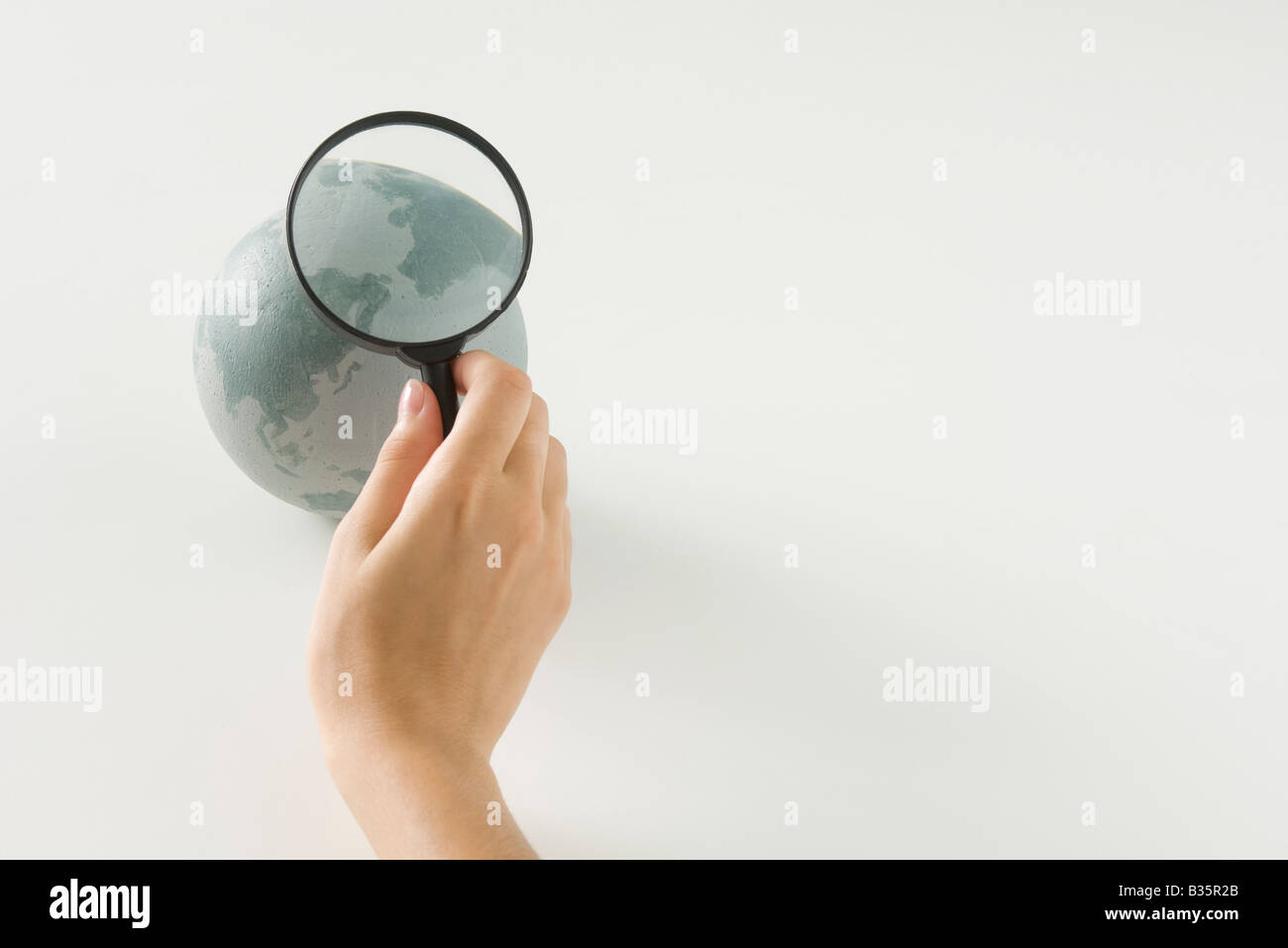 Hand holding magnifying glass over globe, cropped view Stock Photo