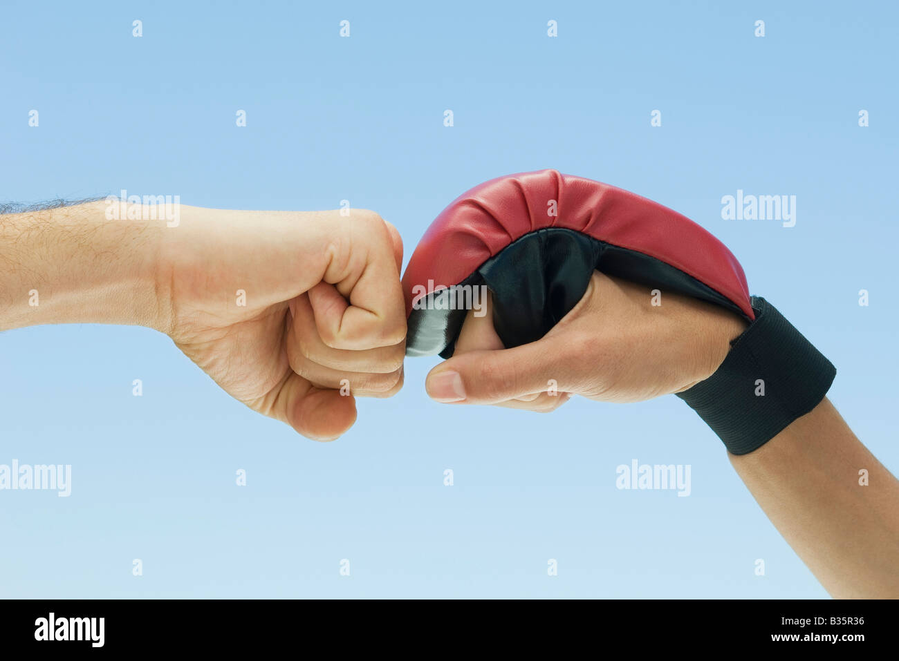 Clenched fist and hand wearing boxing glove bumping together, cropped view Stock Photo