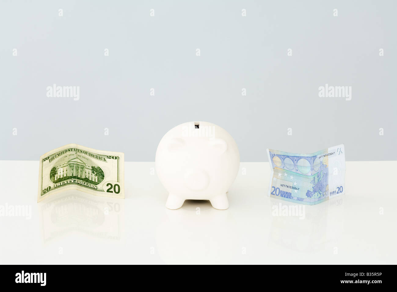 Piggy bank with folded twenty dollar bill to one side and a twenty euro bill on the other side Stock Photo