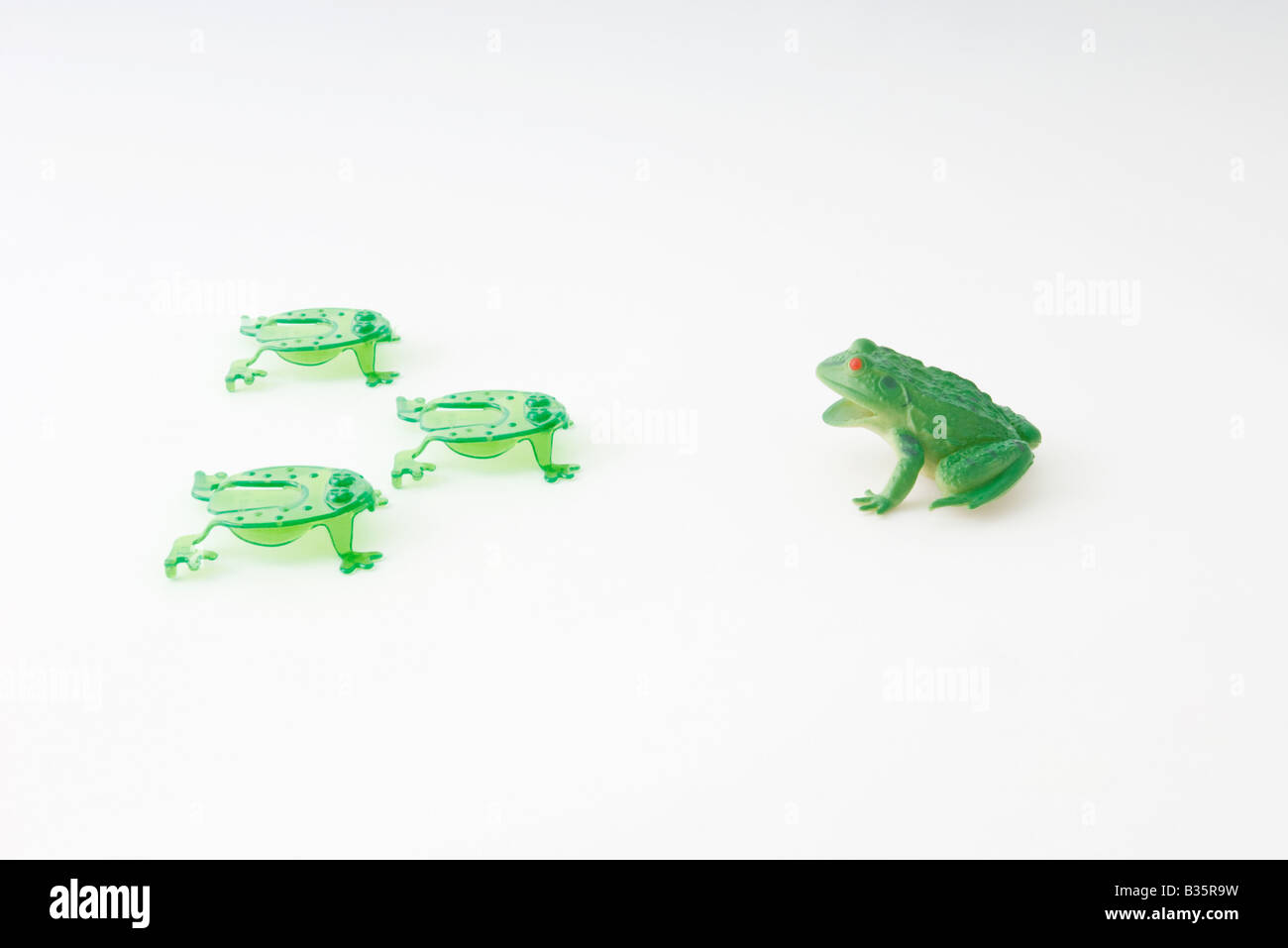 Plastic frog facing group of frog shaped game pieces Stock Photo