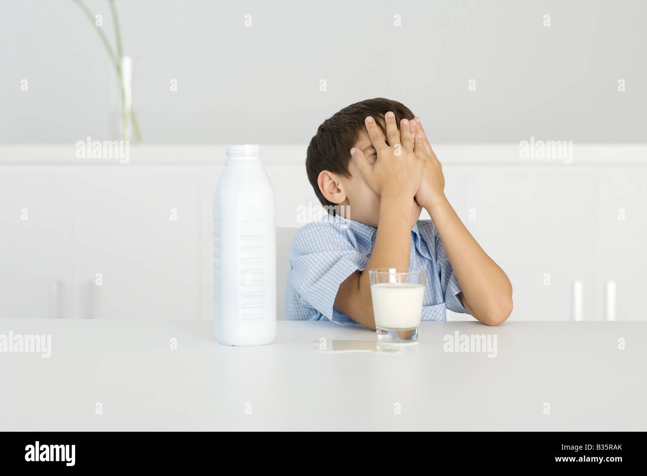 Boy with spilled milk, covering face with hands Stock Photo