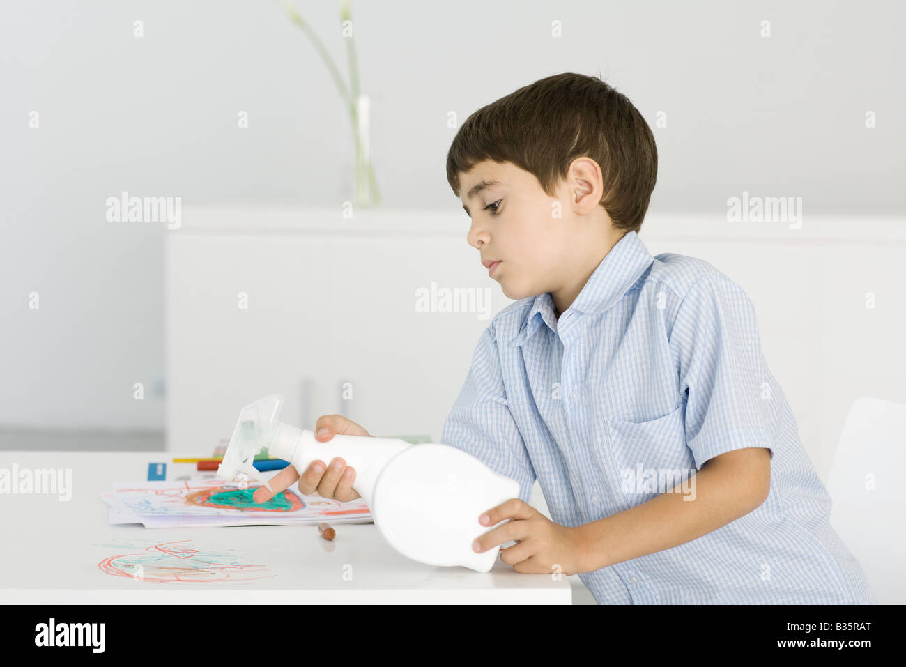 Boy cleaning crayon scribbles off of table, holding spray bottle Stock