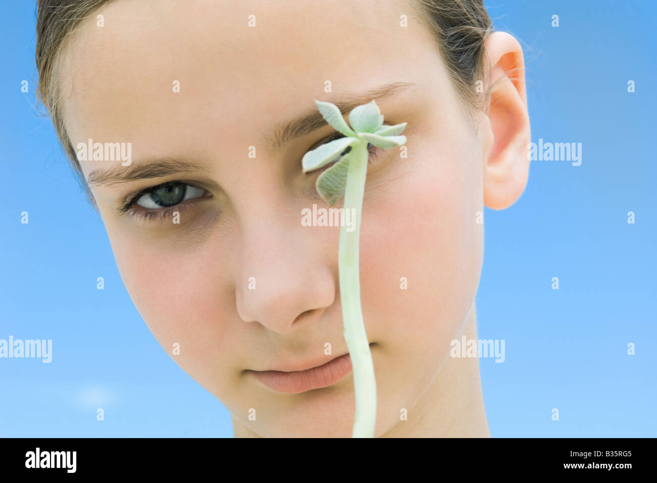 Girl with long stemmed succulent plant obscuring one of her eyes Stock Photo