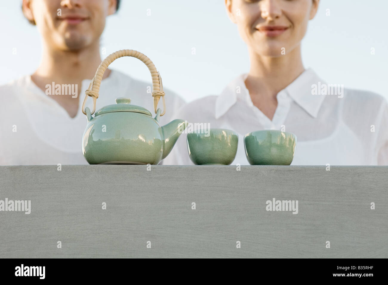 Teapot and tea cups sitting on ledge, cropped view of man and woman