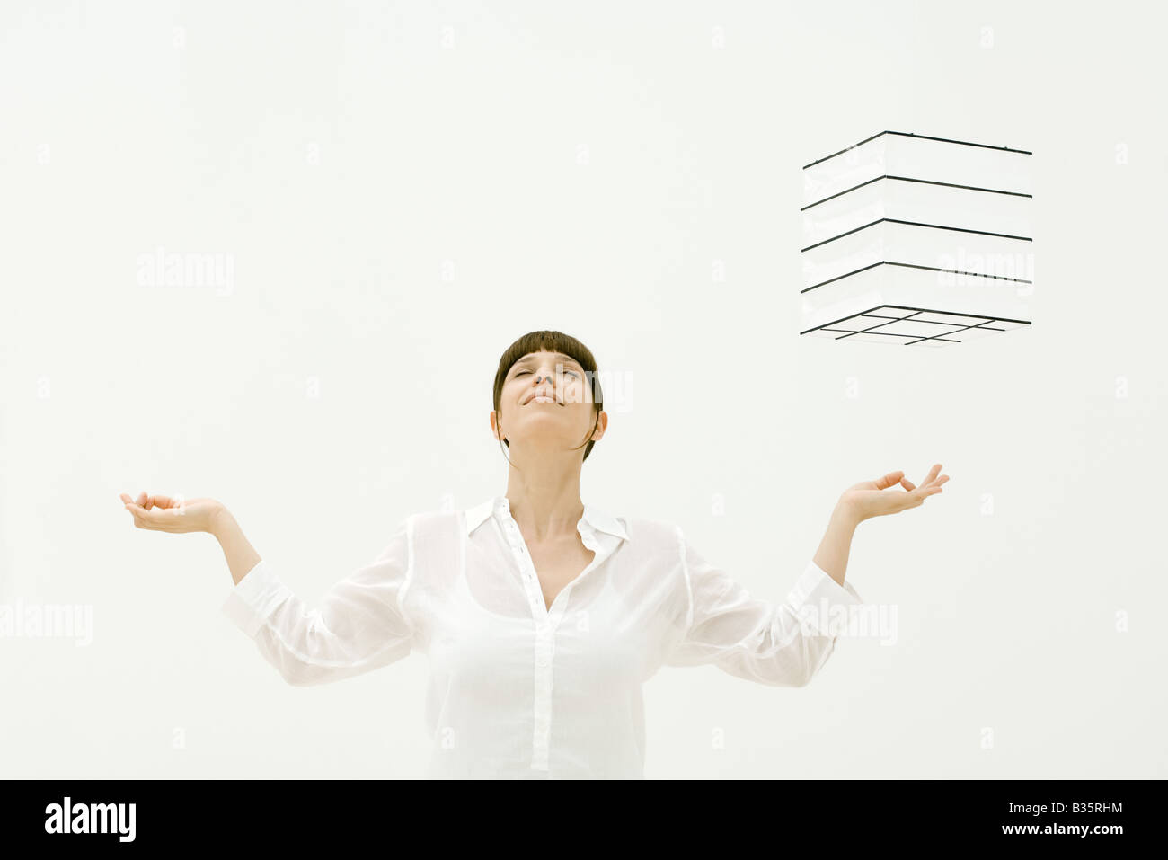 Woman meditating, cube hovering in midair over her left hand, head back, eyes closed Stock Photo