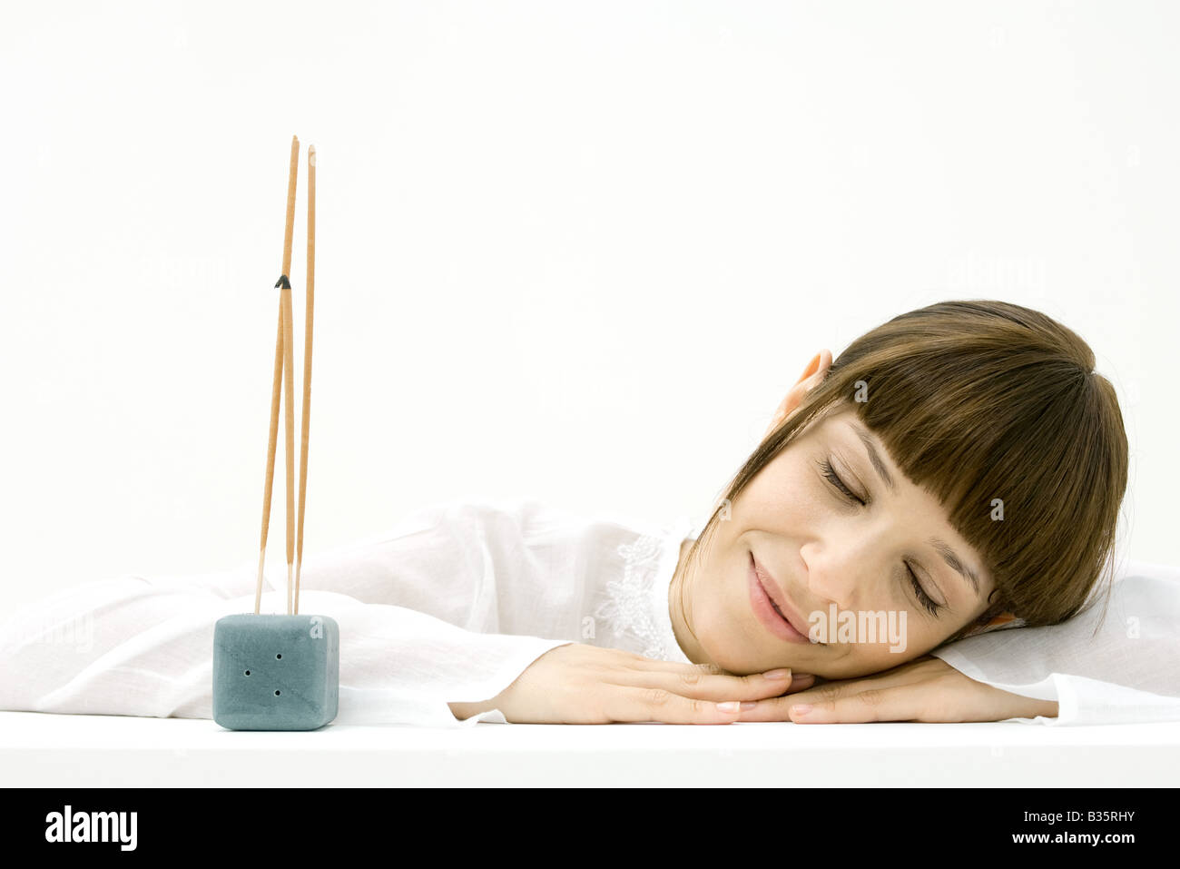 Woman resting head on arm beside incense, smiling with eyes closed Stock Photo