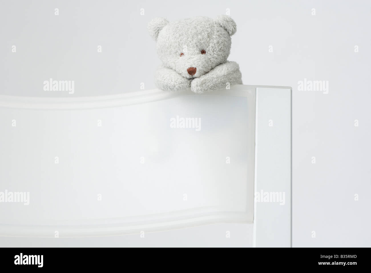 Teddy bear hanging off the back of a chair Stock Photo