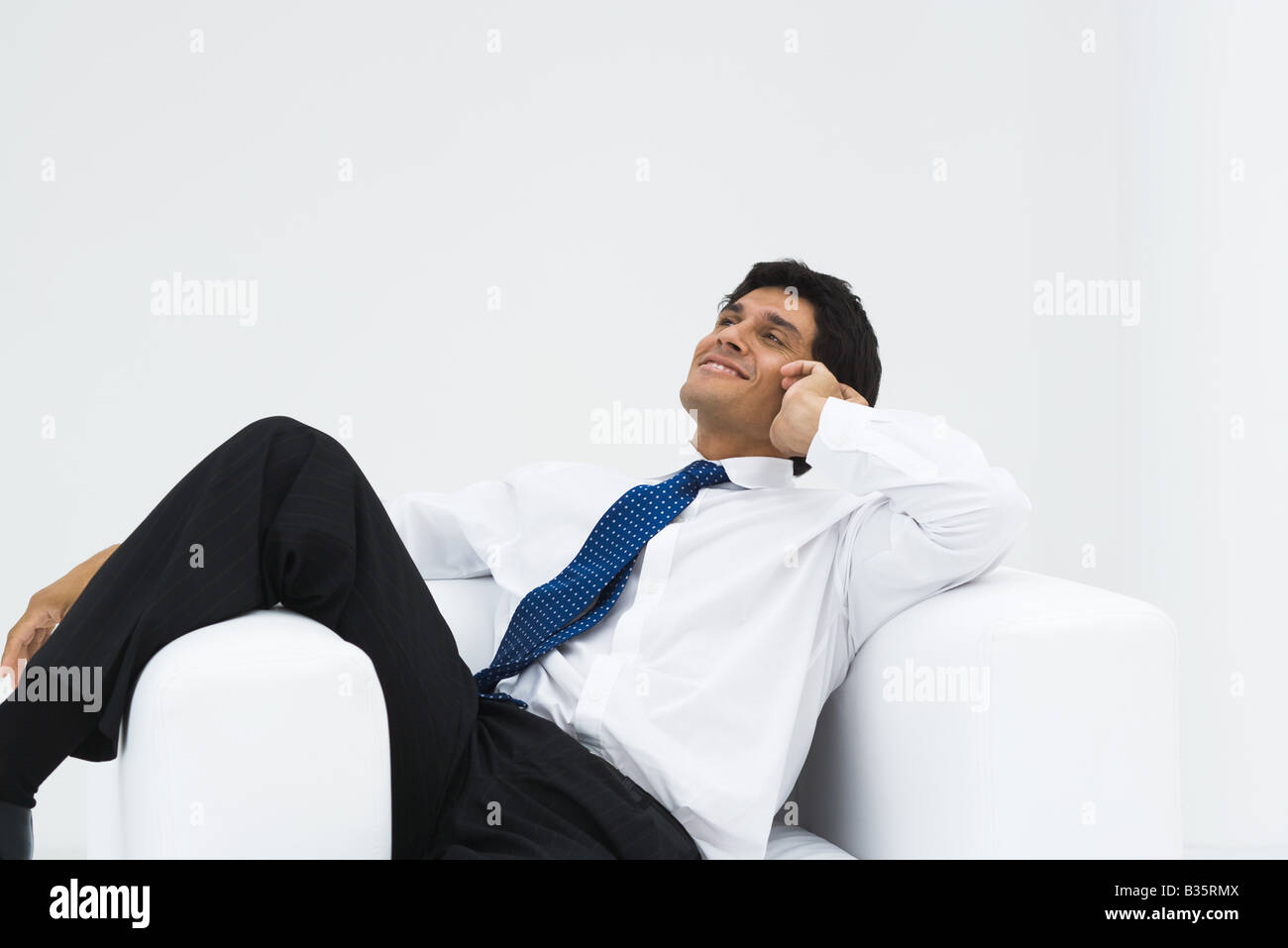 Businessman relaxing in armchair, talking on the phone, smiling Stock