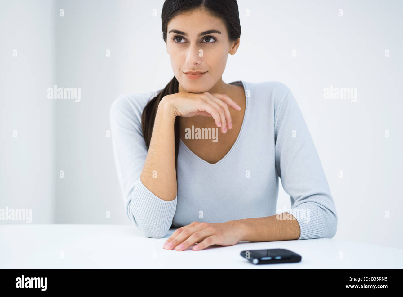 Woman sitting at table with hand under chin, looking away Stock Photo -  Alamy