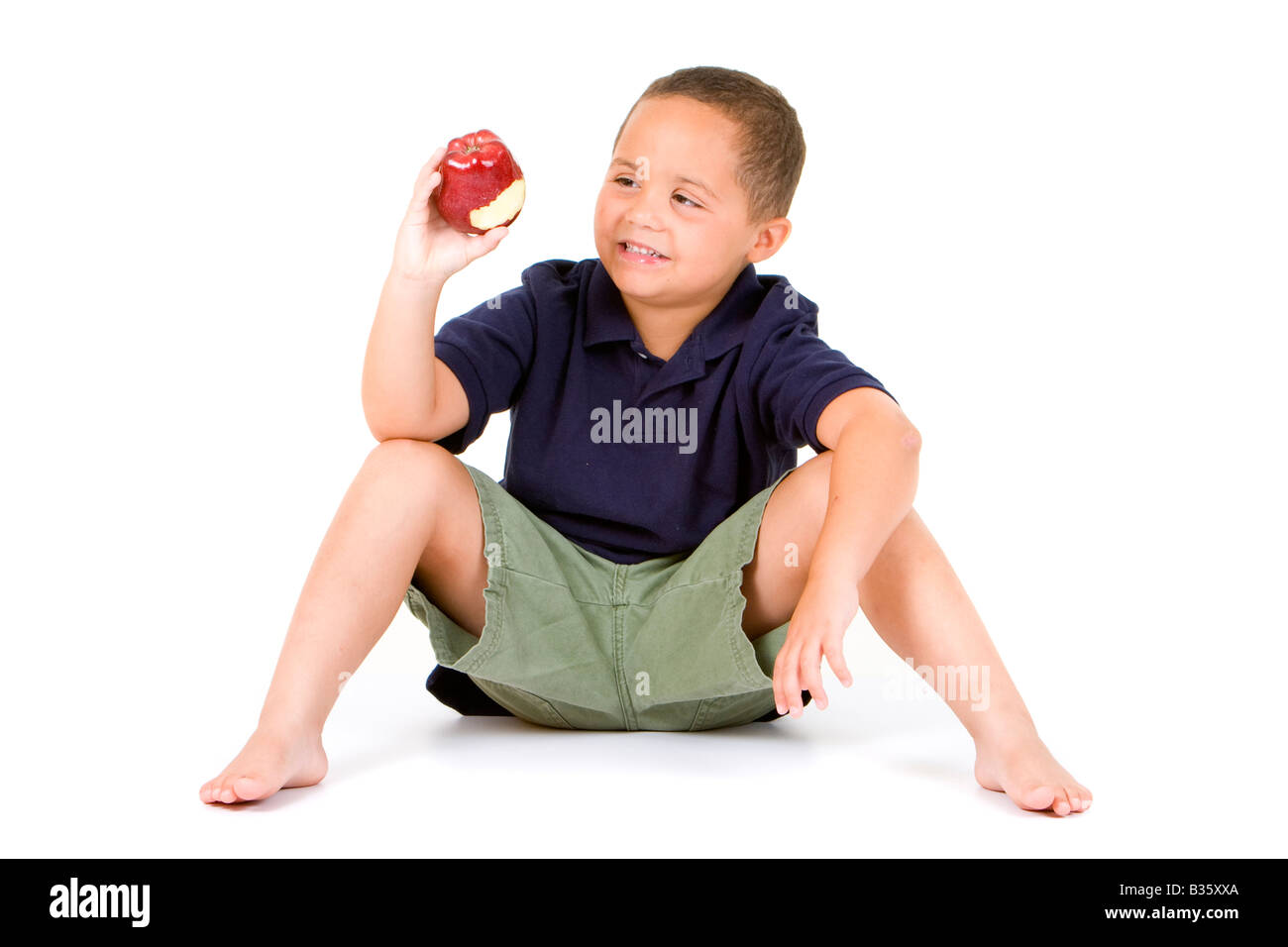 Young Latino boy sitting on white background eating a red apple Stock Photo