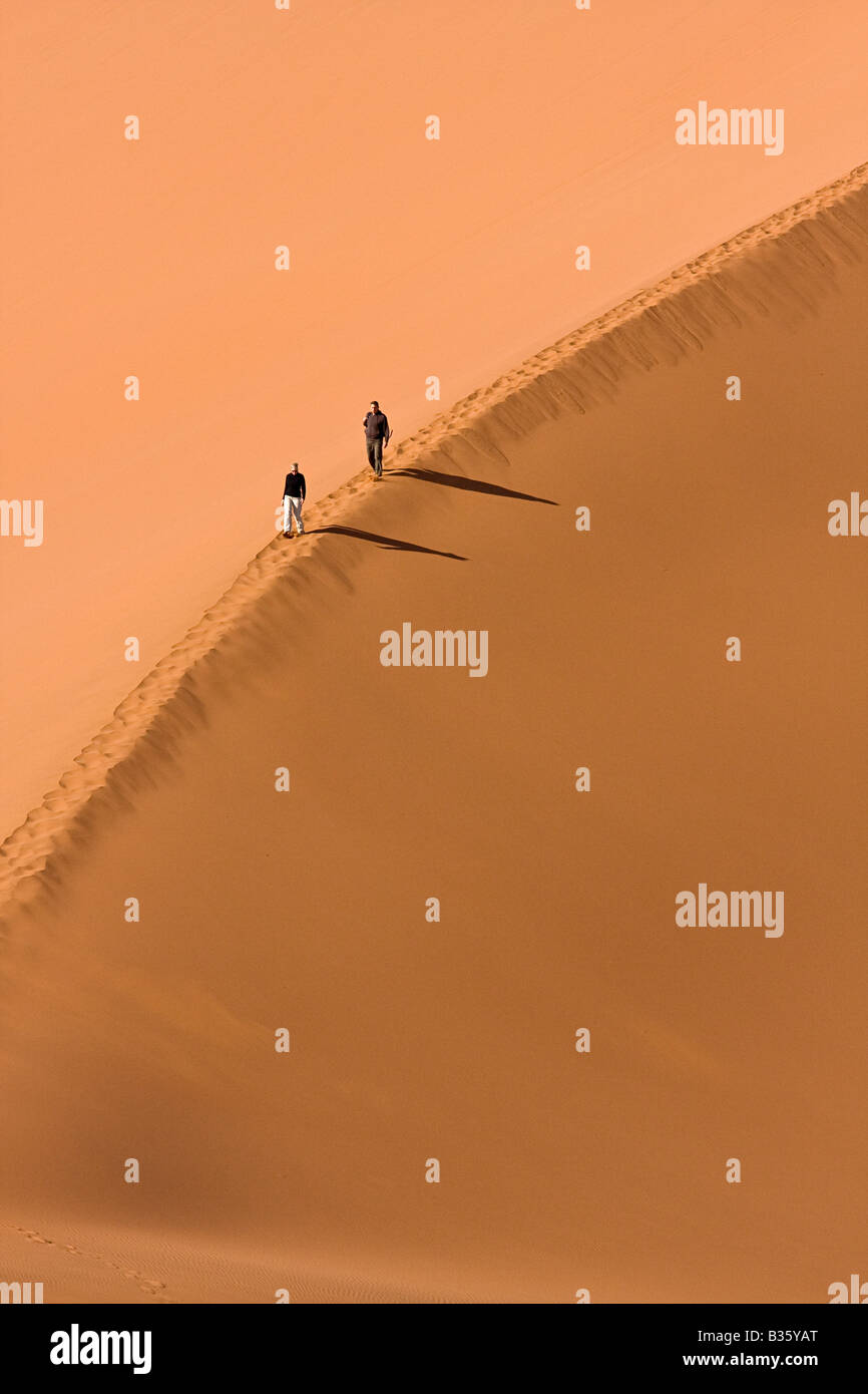 Man and woman walk atop sand dunes of Sossusvlei in the Namib Naukluft Park of south central Namibia of Africa Stock Photo