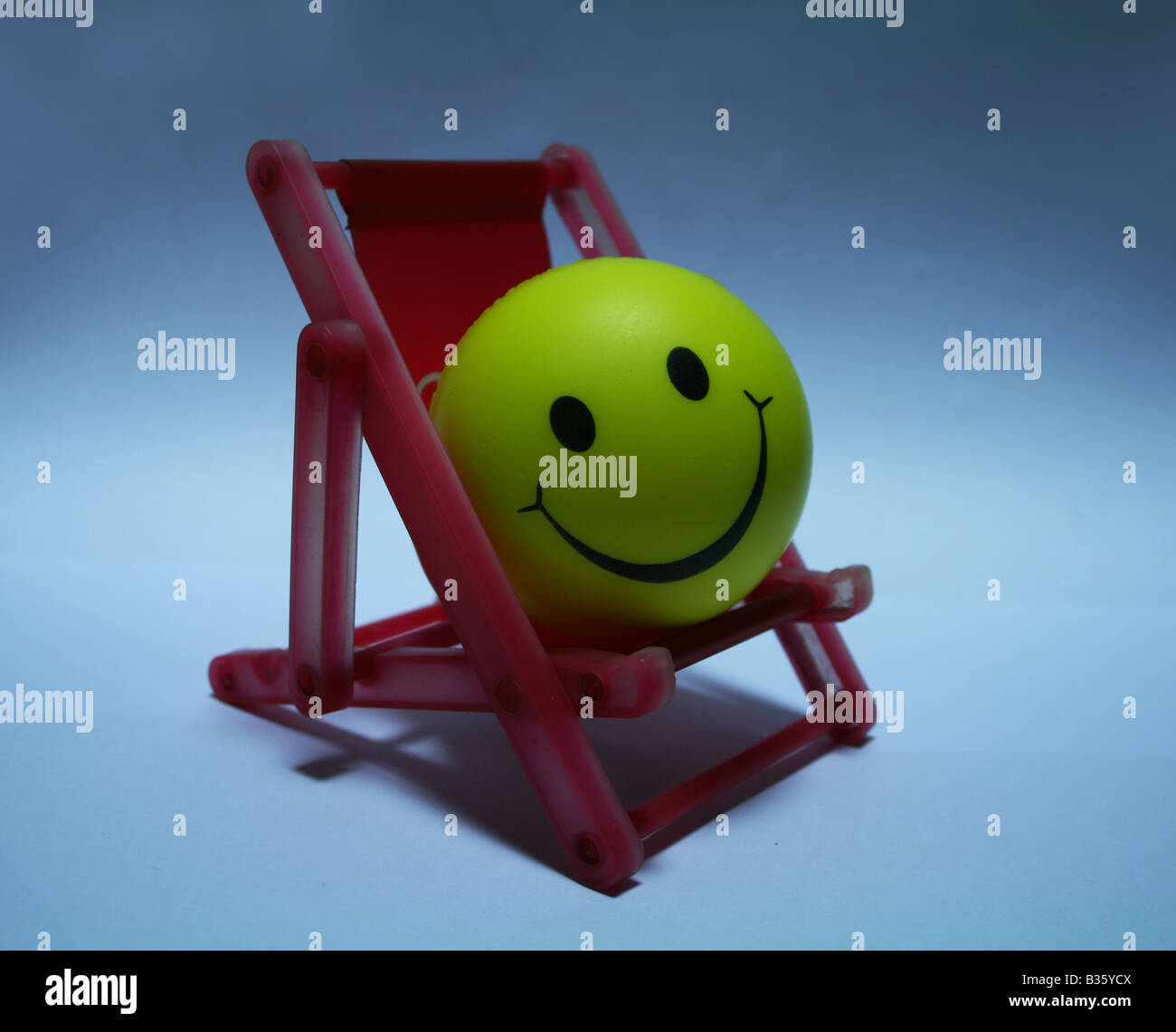 Yellow Smiley ball enjoying by relaxing himself on a red Easy Chair in the moonlight thinking of some fond memories Stock Photo