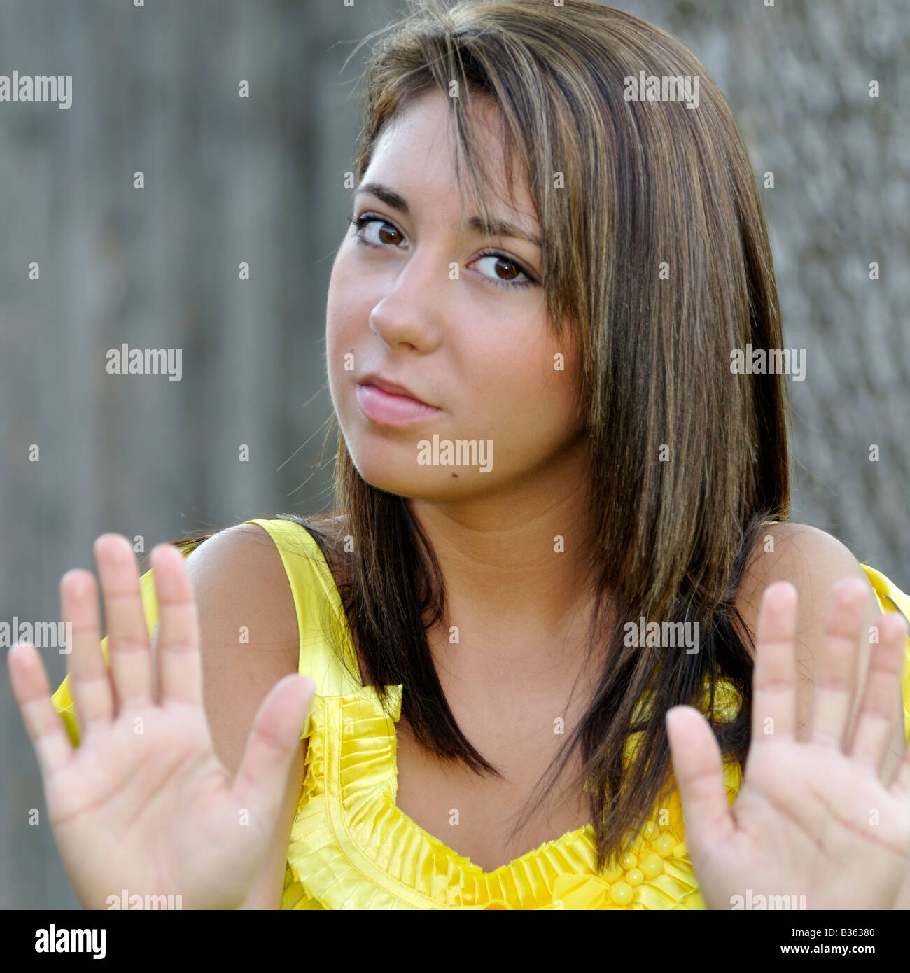A 16 year old pretty caucasian girl, brown hair, brown eyes, holds her hands out in a warding off gesture. Conceptual image. Stock Photo