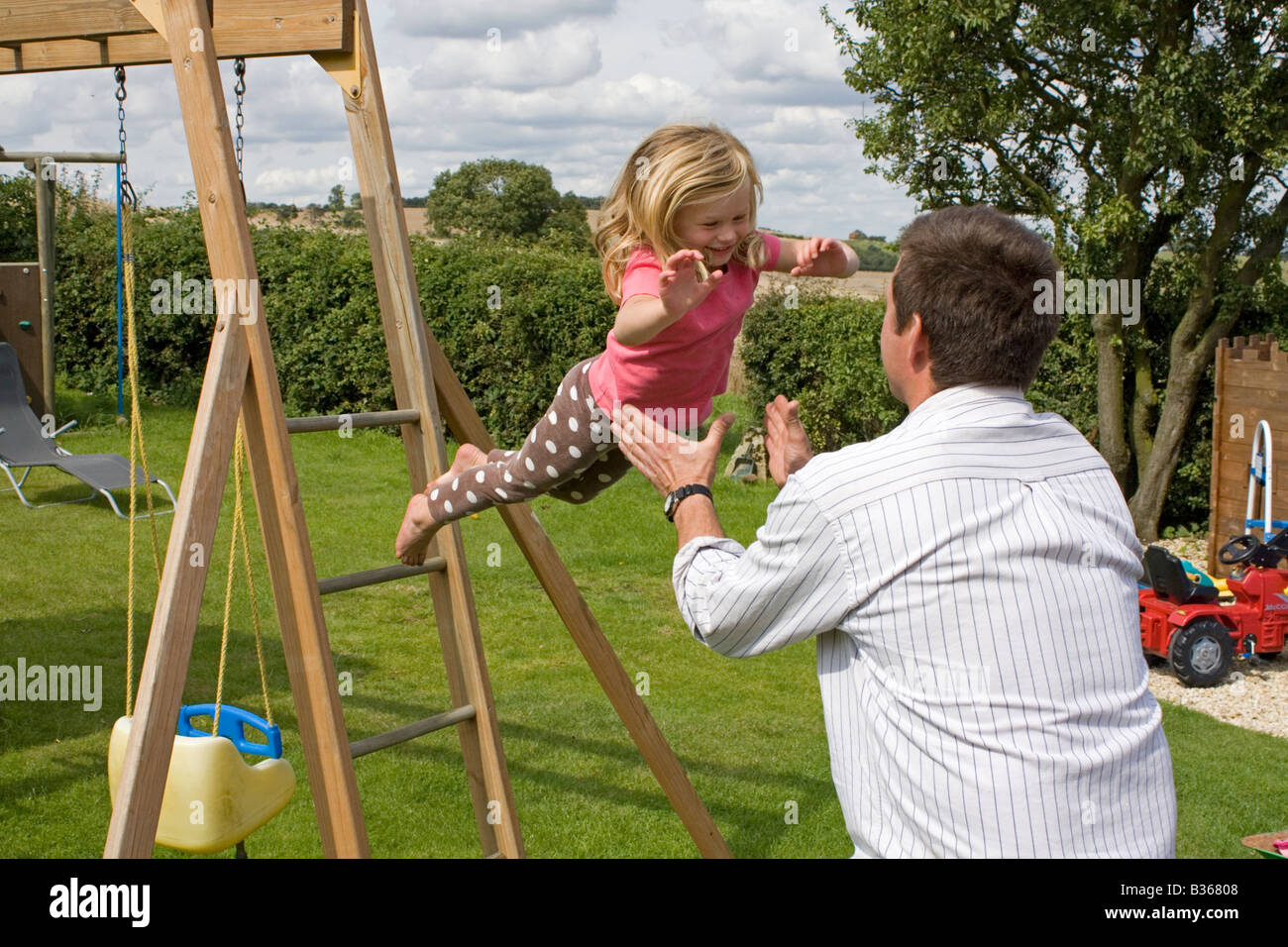 Child jumping into fathers arms from climbing frame Stock Photo Alamy