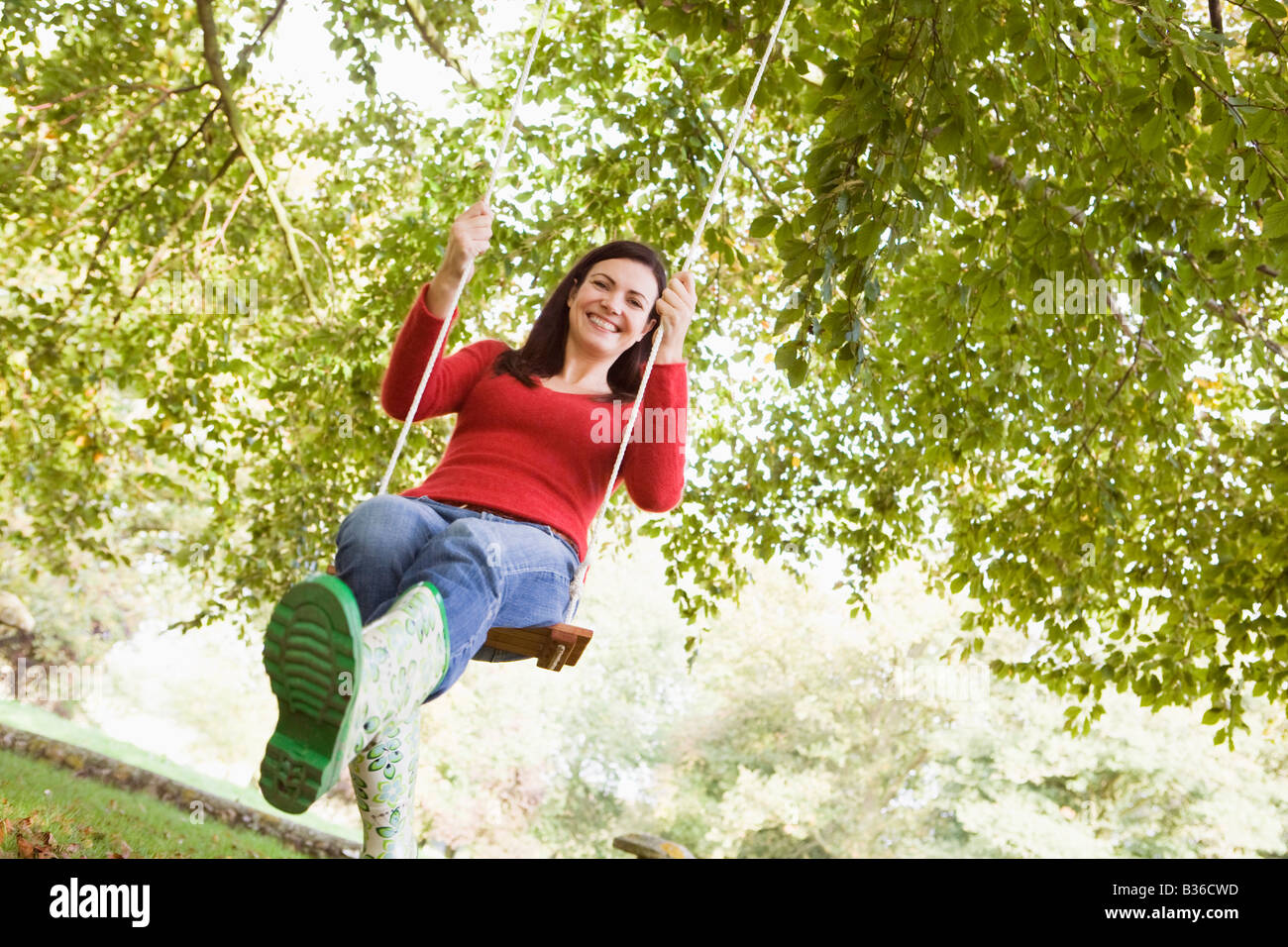 Woman outdoors on tree swing smiling (high key/selective focus) Stock Photo