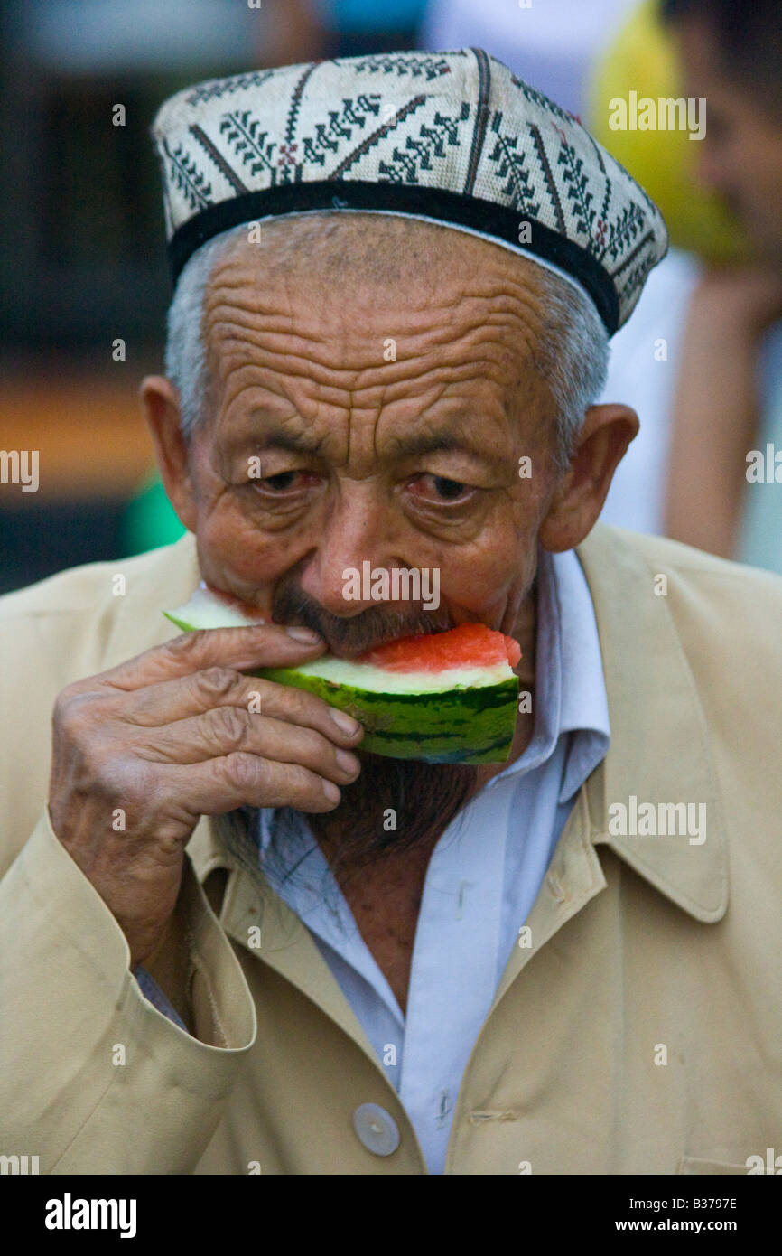 Elderly Uyghur Man Eating Watermelon in Old Kashgar in Xinjiang Province China Stock Photo