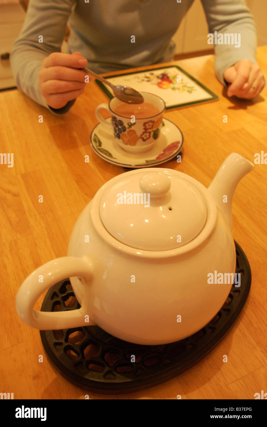 Teapot with woman stirring cup of tea at kitchen table Stock Photo