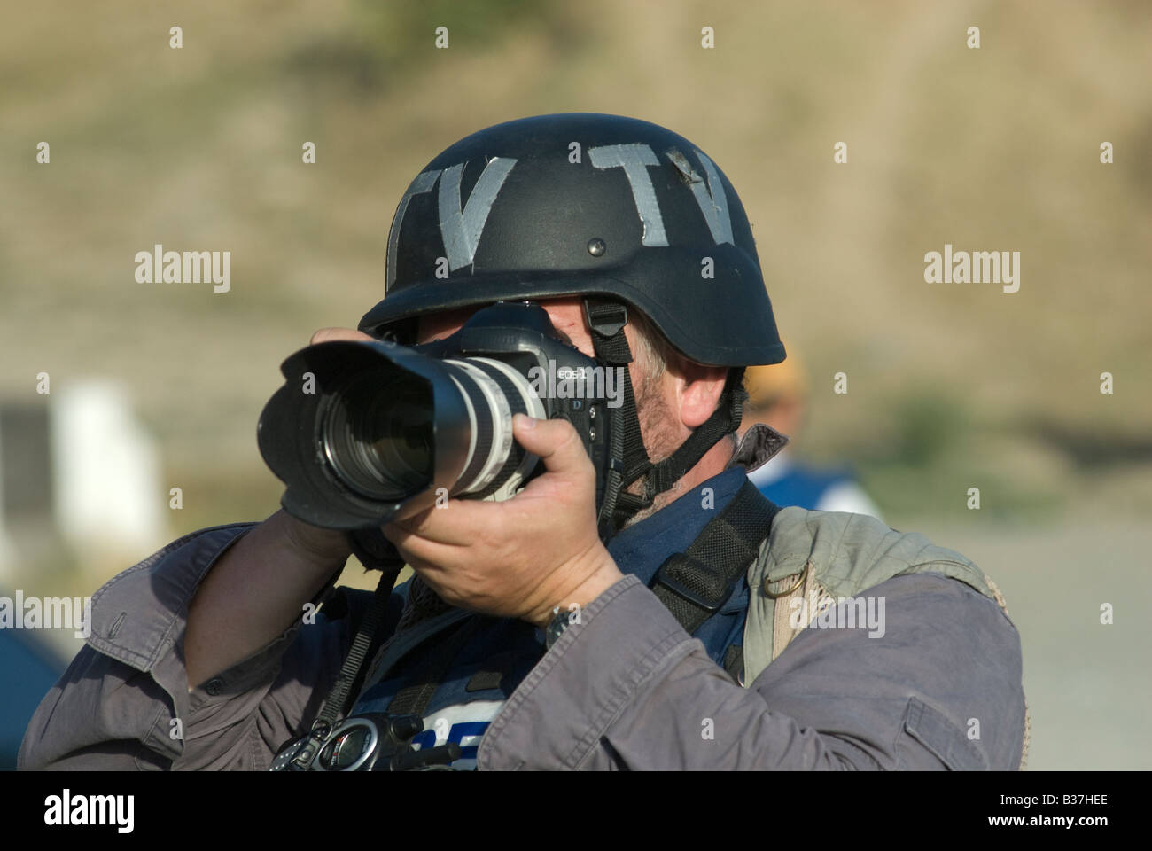 A photojournalist wearing a helmet marked 'TV'  takes a photo with a Canon DSLR camera during the Russo-Georgian War Stock Photo