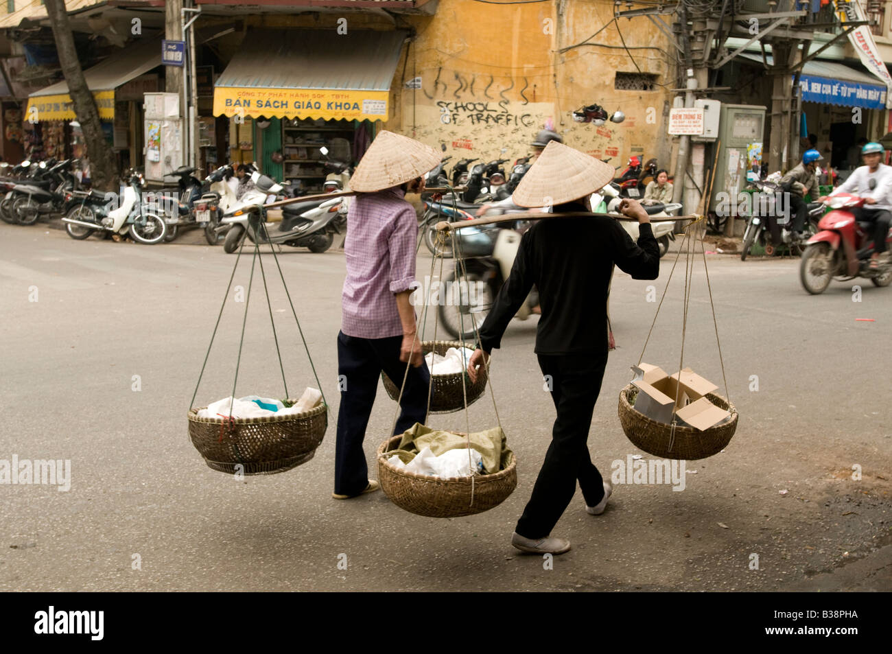 Two women traders with shoulder pole baskets walking up a street in Hanoi Vietnam Stock Photo