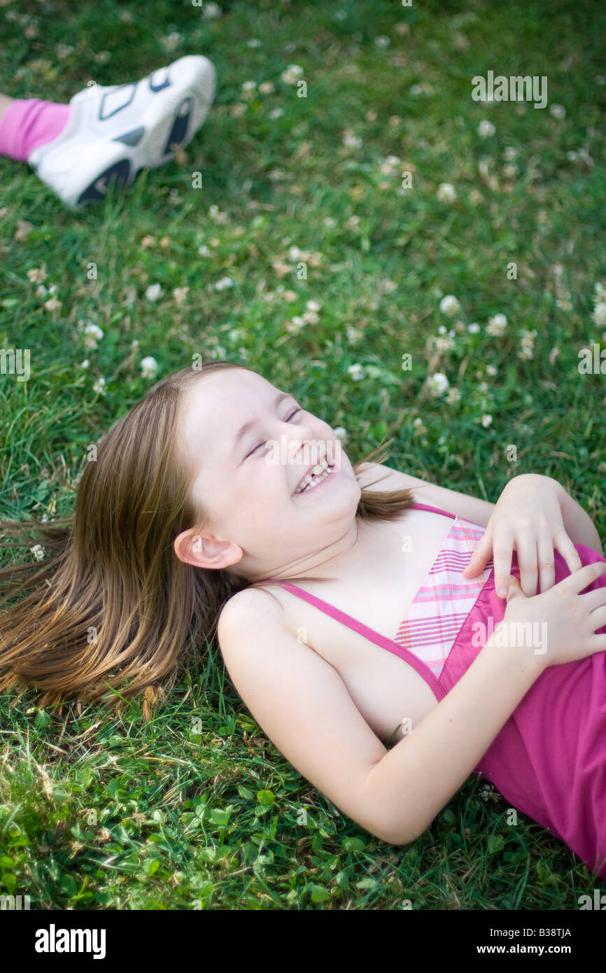 Young girl rolls in a grassy meadow giggling with her eyes closed in