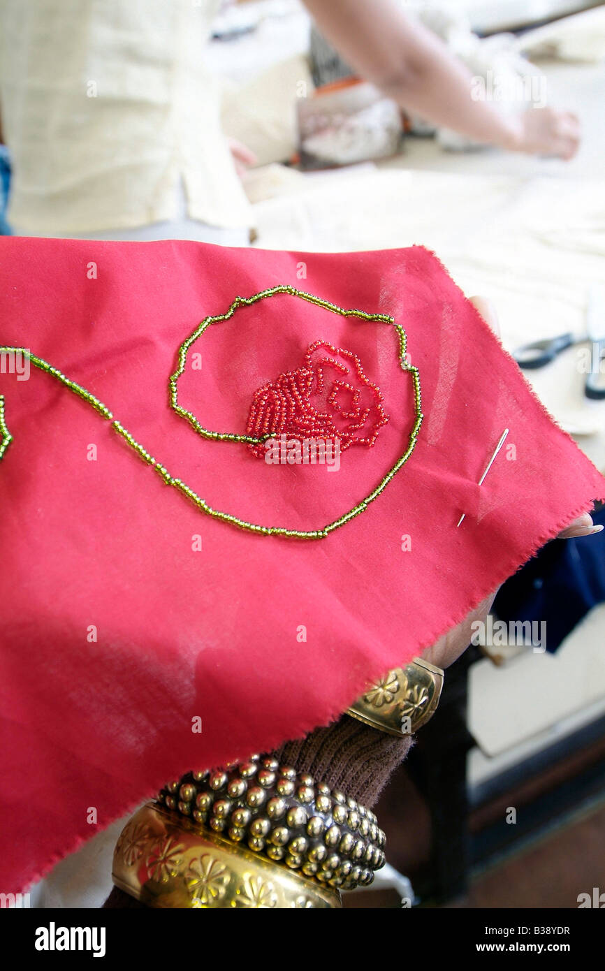 Close-up of a piece of hand-embroidered red silk being stitched with red and gold beads Stock Photo
