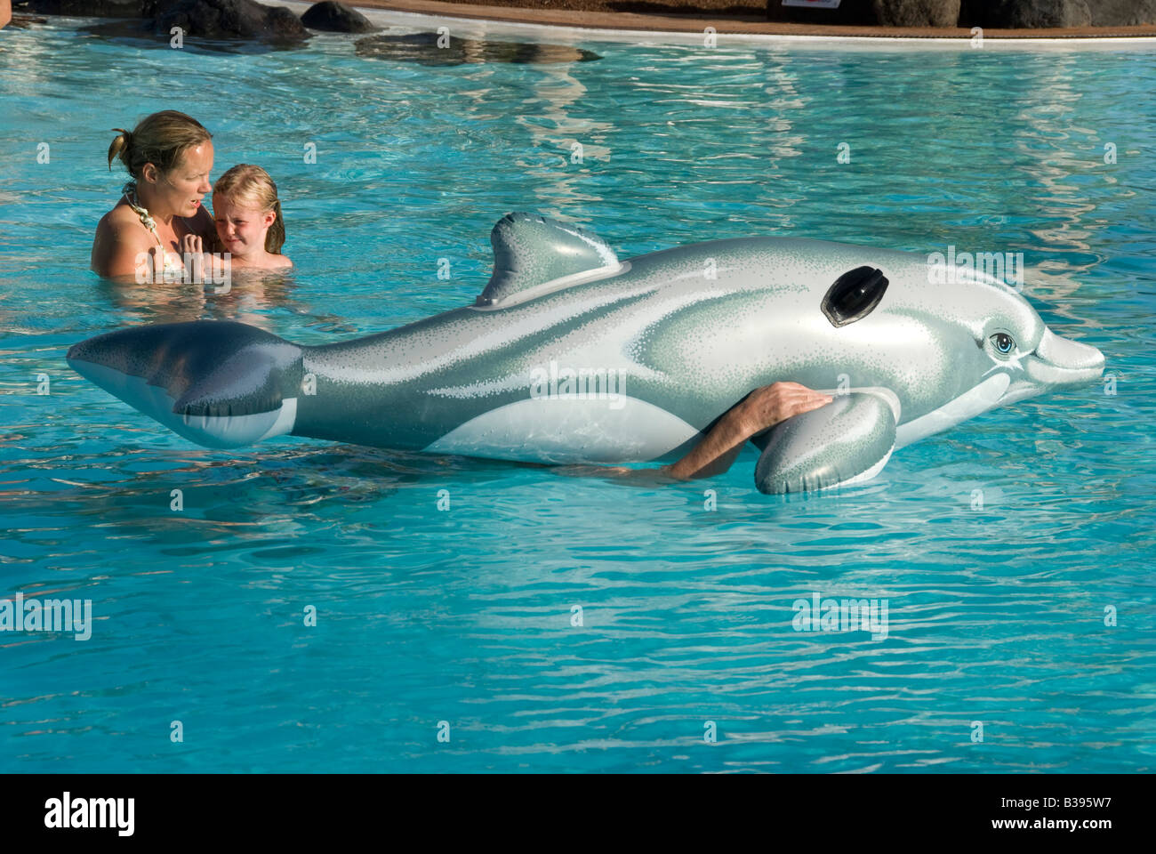 Mother and daughter in swimming pool with inflatable dolphin guided by man under water Stock Photo