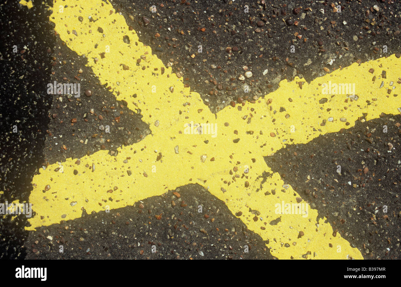 Uneven yellow lines painted on tarmac surface as part of a No Parking grid detailed as X with earlier paint covered Stock Photo