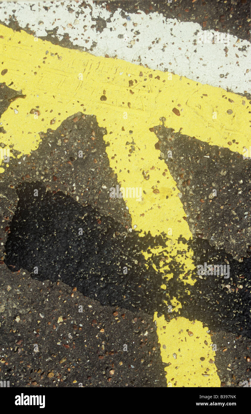 Detail of uneven yellow and white lines painted on tarmac surface as part of a No parking grid with earlier paint covered Stock Photo