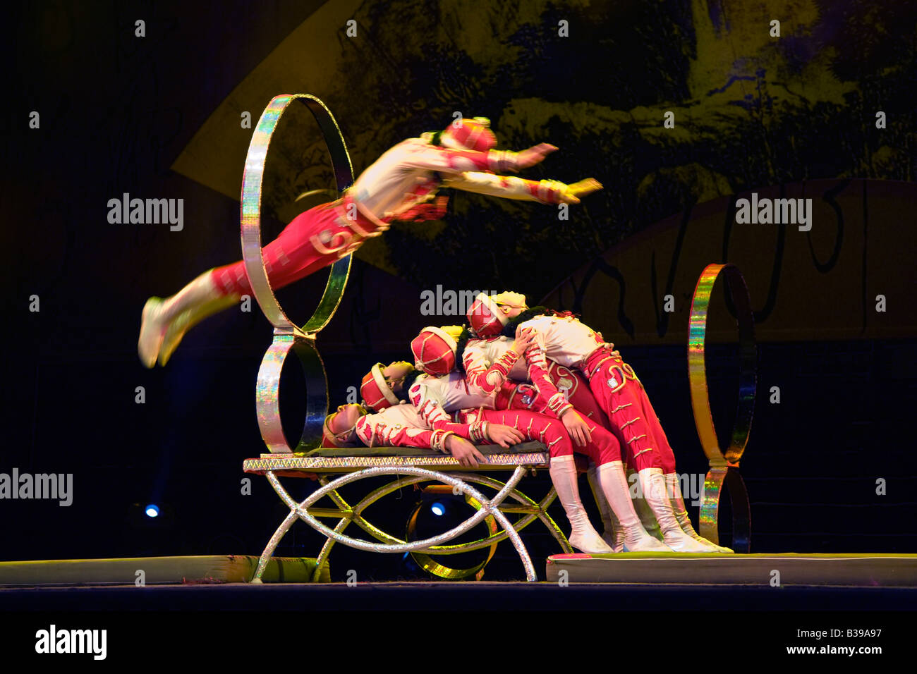 Acrobat in mid air jumps through hoop and over four others at